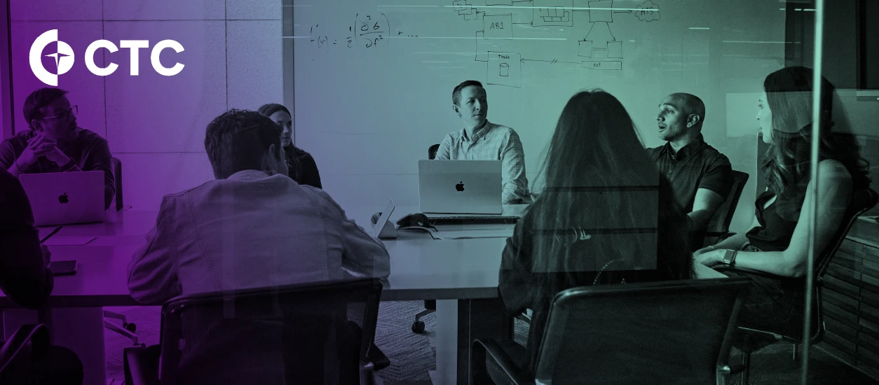 Colleagues meet around a conference table with laptops while one speaks, with a diagram-covered whiteboard behind them. A CTC logo is in the upper left corner.